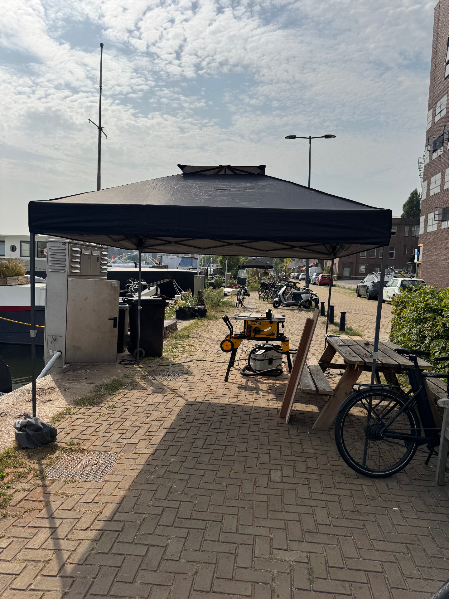 Mobiele werkplaats van De Waterwerf aan de kade: partytent met gereedschap en materiaal naast een woonschip