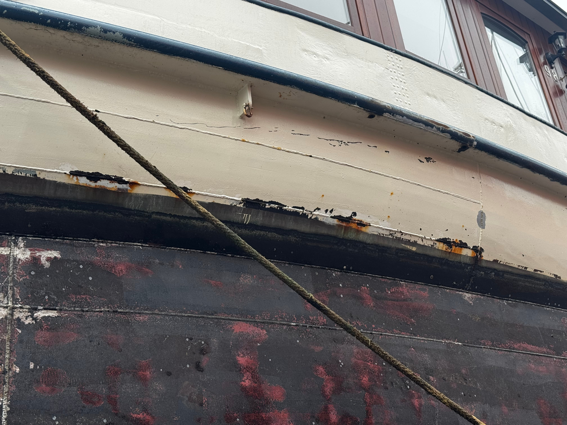 Woonschip romp met slijtage aan kabelgoot en verweerd schilderwerk: onderhoud dat aan de kade kan worden voorbereid