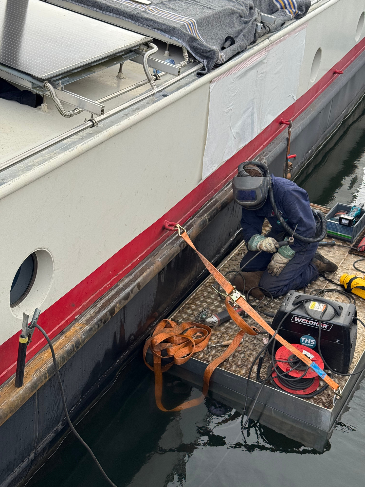 Monteur voert laswerk uit aan het berghout van een woonschip vanaf een werkvlot